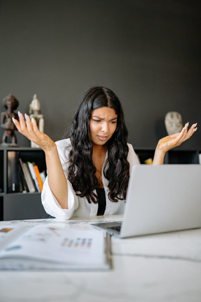 A frustrated businesswoman sits at her office desk, puzzled over her laptop.